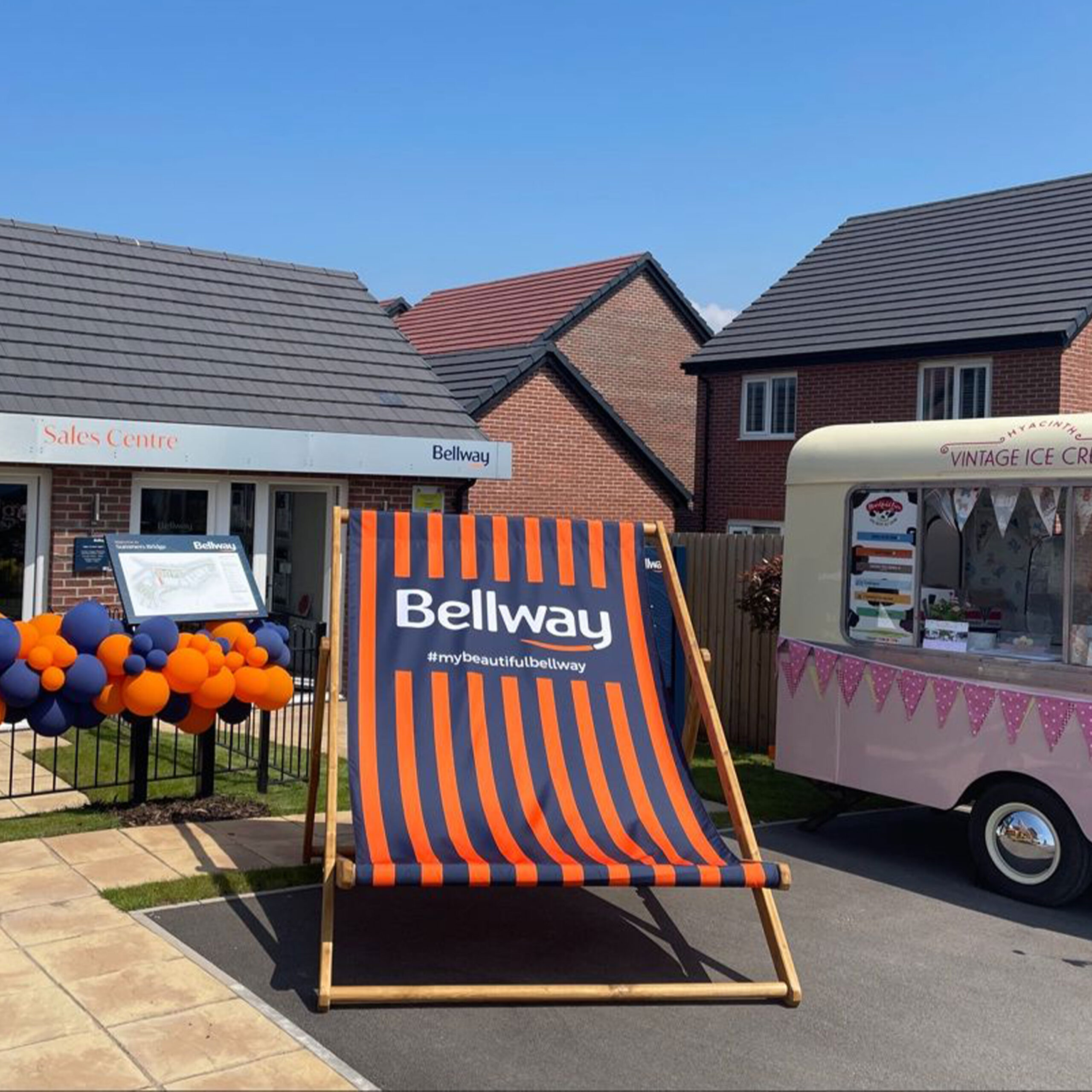 Giant custom-printed deckchair with Bellway branding, positioned outside a sales centre at an outdoor promotional marketing event.