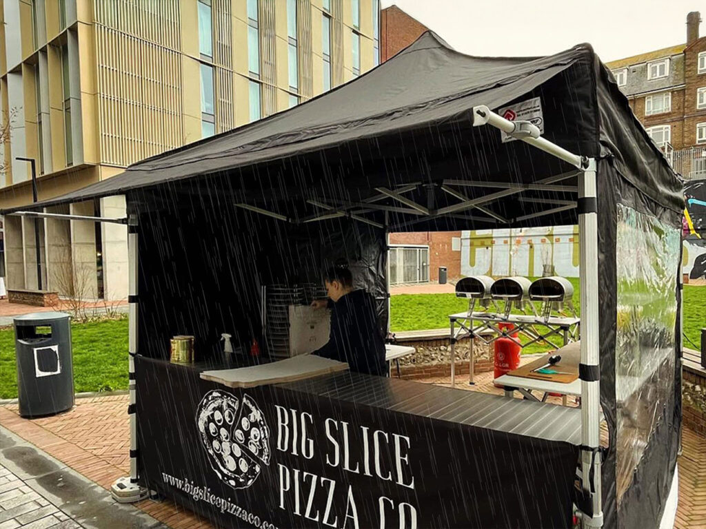 a pizza company using their pop up gazebo from surf & turf instant shelters with a rain awning attachment protecting the store front