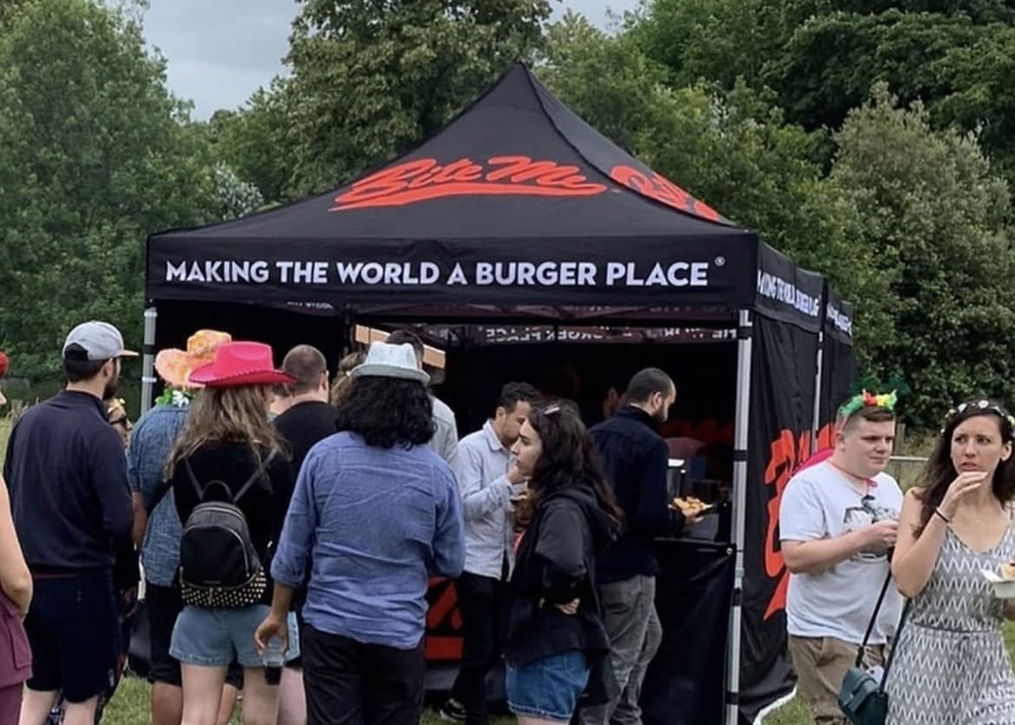 Custom printed festival gazebo in black and red for Bite Me Burger, showcasing a branded catering pop-up tent with a crowd of hungry event-goers at a summer festival.